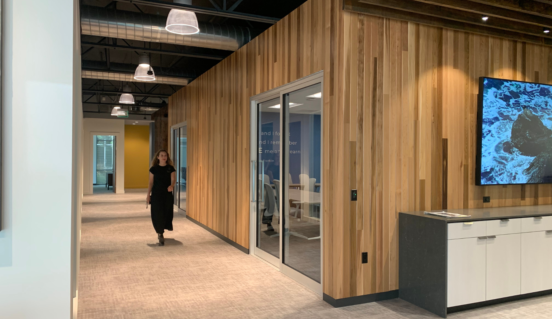 San Diego interior design office hallway, person walking by wood walls, glass door and overhead lighting