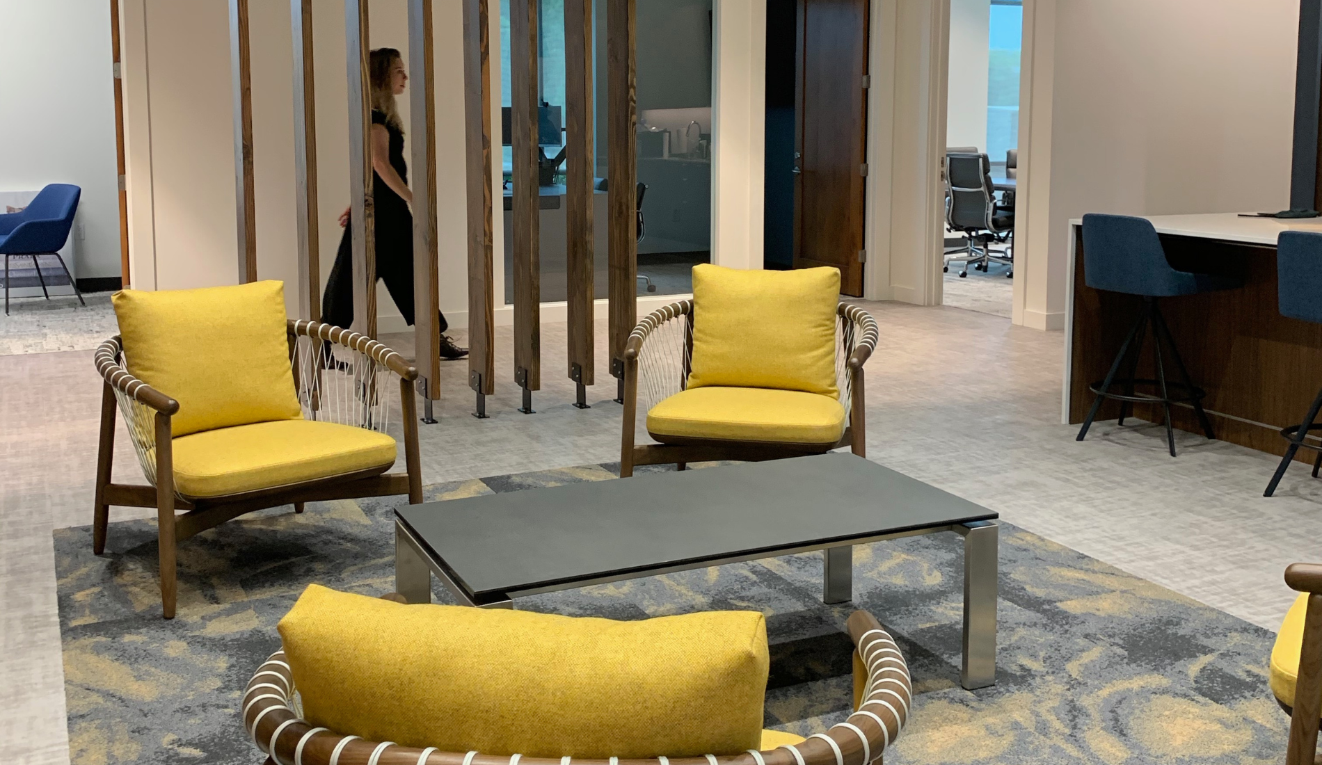 san diego interior design of office space with yellow chairs, rug, table, and person walking through hallway