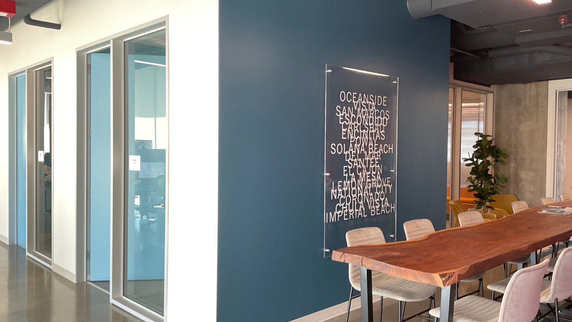 Commercial office interior design, blue wall with text wall decor behind wood meeting table and chairs, individual offices with glass doors and white walls