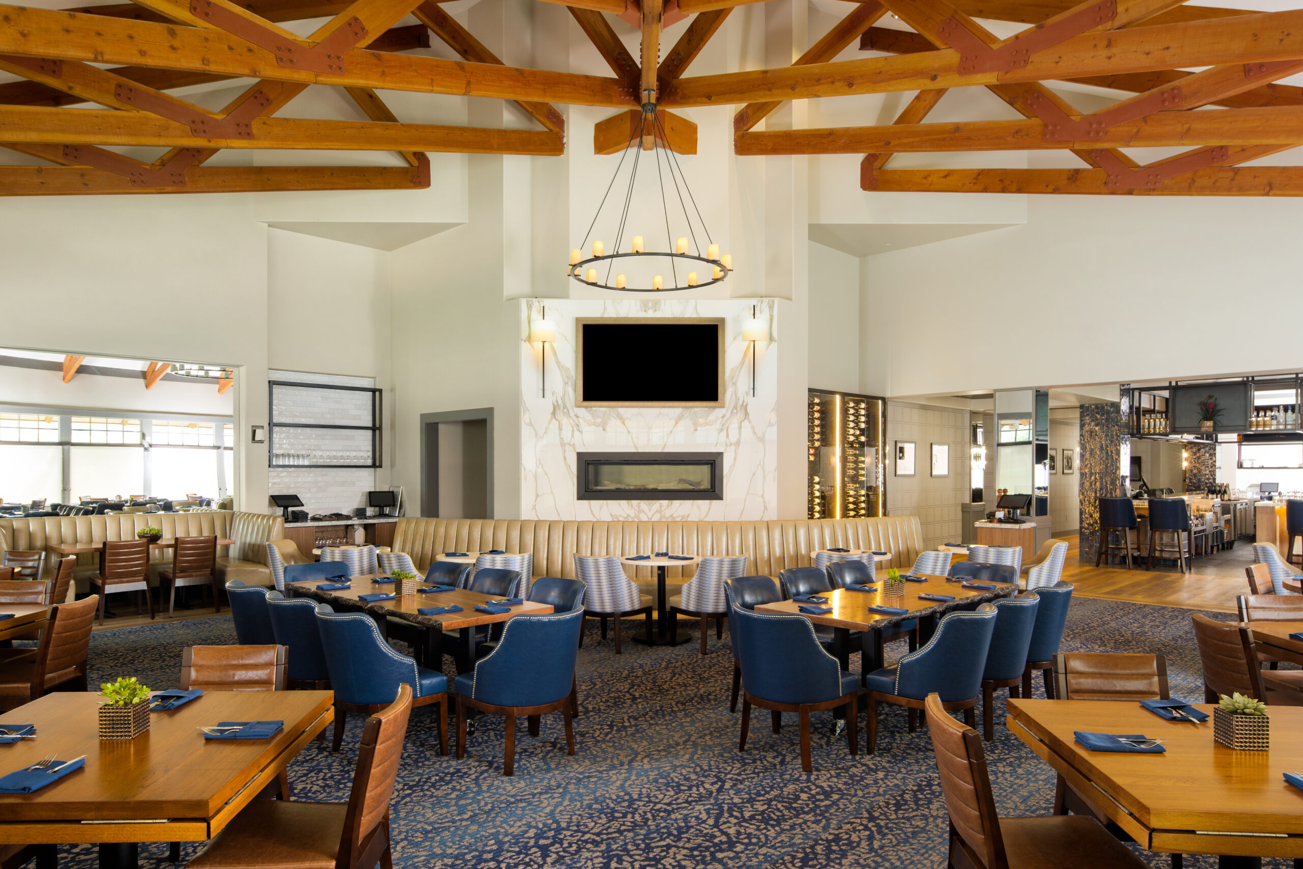 Upscale country club bar and restaurant interior design and furniture, seating area with fireplace, blue chairs, wood beams, booths