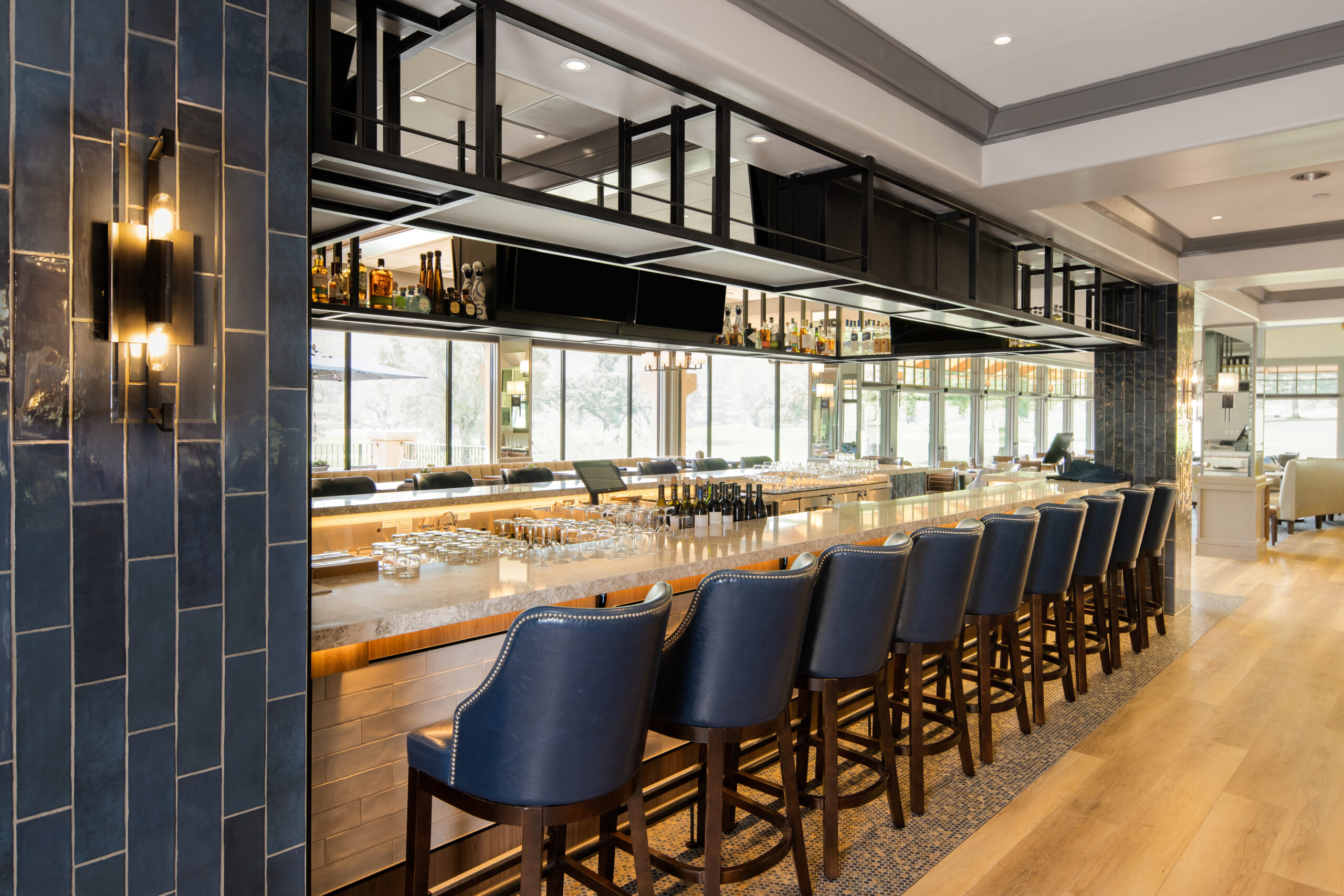 Sophisticated country club bar and restaurant interior design, blue bar seating with shelving, glasses