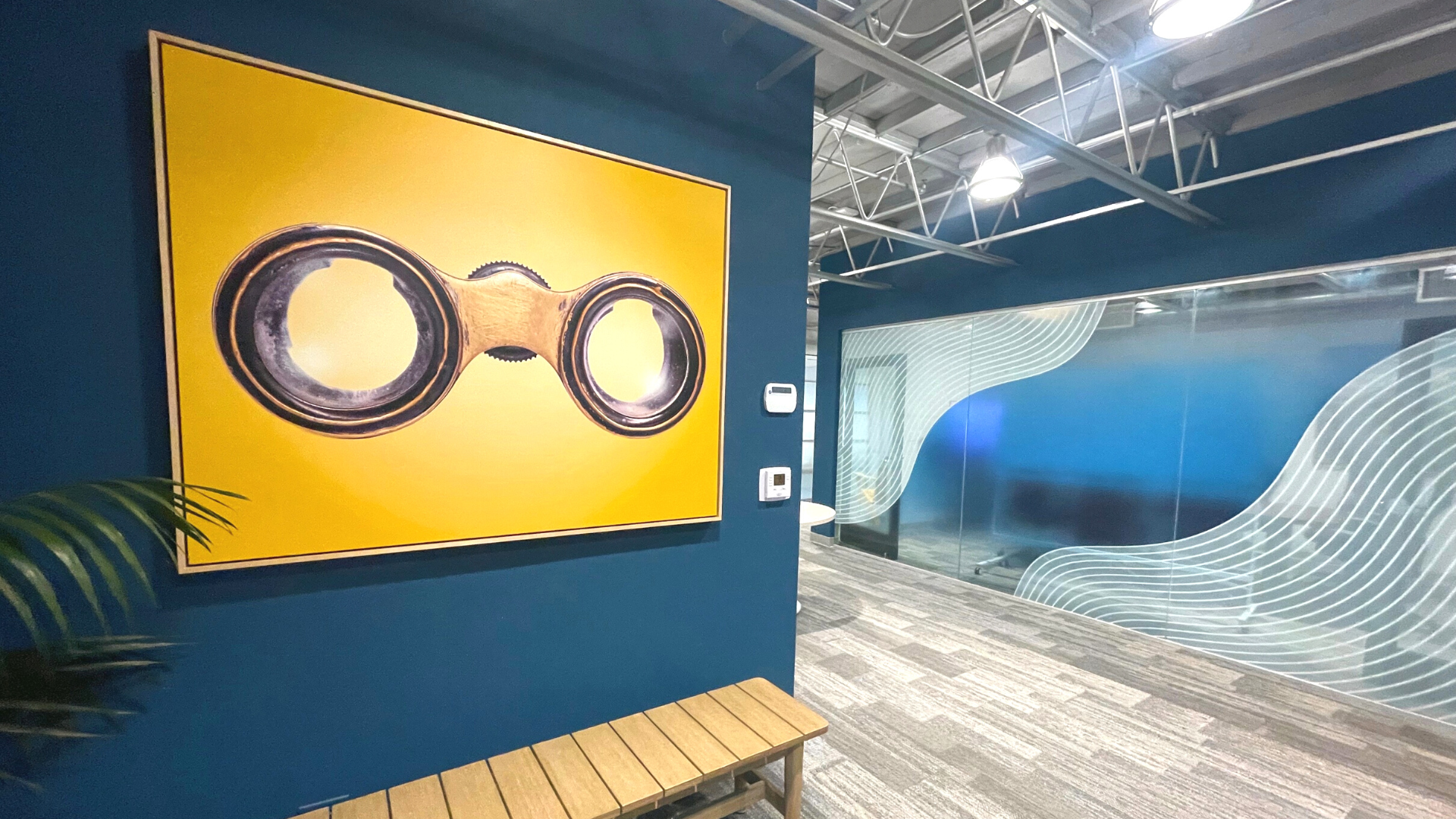 San Diego interior design office space lobby hallway with bench, framed yellow image of binoculars, and conference room with blue and white detailing